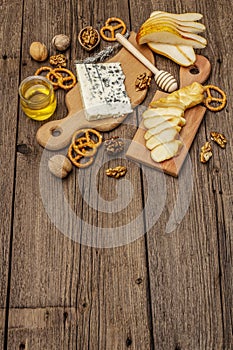 Cheese plate antipasti with smoked and blue cheese, crackers, honey, walnuts and ripe pear. Traditional snack recipe idea. Wooden