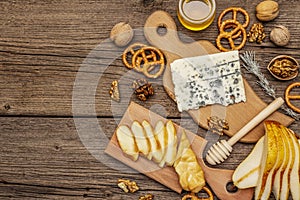 Cheese plate antipasti with smoked and blue cheese, crackers, honey, walnuts and ripe pear. Traditional snack recipe idea. Wooden