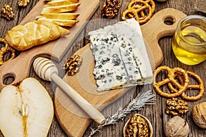 Cheese plate antipasti with smoked and blue cheese, crackers, honey, walnuts and ripe pear. Traditional snack recipe idea. Wooden