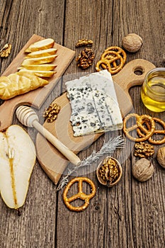 Cheese plate antipasti with smoked and blue cheese, crackers, honey, walnuts and ripe pear. Traditional snack recipe idea. Wooden