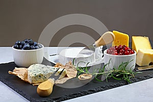 Cheese plate. Assortment of cheese with walnuts, cranberry, rosemary sprig, blueberries on a stone plate. Cheese Serving Knife. cl