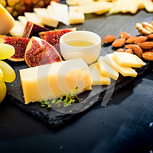 Cheese plate. Assortment of cheese with walnuts, almonds, grapes, figs, strawberries, blueberries and honey on a stone