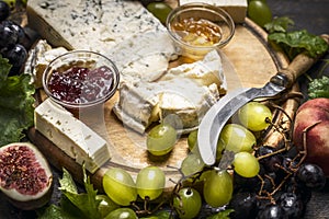 Cheese plate with Gorgonzola and Camembert cheese knife honey jam light and dark grapes a wooden cutting board close up