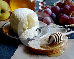 Cheese on a plate, honey, bread on paper, ripe grapes, fork, napkin on a dark background