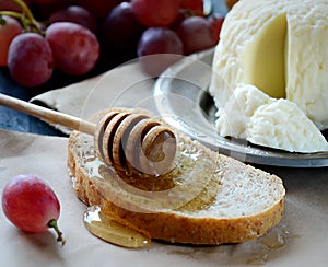 Cheese on a plate and honey, ripe grapes, bread,dipper, napkin on a light background