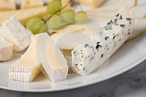 Cheese plate platter with selection Edamer, Parmesan, goat, blue and cream cheese, peer and grapes on marble background photo