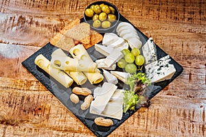 Sýrový talíř, sada různých sýrů na černém talíři s hrozny zelené olivy hranolky nuts.copy space