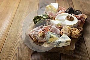 Cheese plate, various types of cheeses, grapes, walnuts and honey and prosciutto. Wooden cutting board