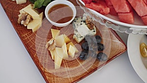 Cheese plate with walnuts, grapes and small vase of honey on the table.