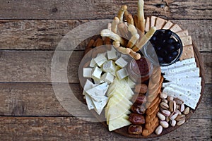 Cheese plates served with grissini, crackers, dates, jam, olives and nuts on wooden background