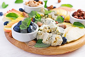 Cheese platter with assorted cheeses, blueberry, apples, nuts on white table.