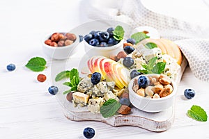 Cheese platter with assorted cheeses, blueberry, apples, nuts on white table