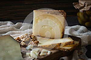 Cheese platter of chopped Spanish hard cheese manchego and sliced Italian pecorino toscano on wooden board with walnuts