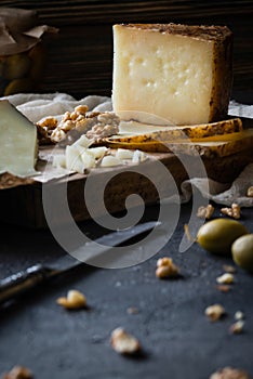 Cheese platter of chopped Spanish hard cheese manchego and sliced Italian pecorino toscano on wooden board with walnuts