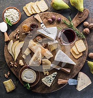 Cheese platter with different cheeses, fruits, nuts and wine on stone background. Top view. Tasty cheese starter