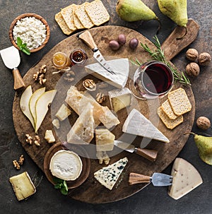 Cheese platter with different cheeses, fruits, nuts and wine on stone background. Top view. Tasty cheese starter