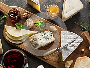 Cheese platter with different cheeses, fruits, nuts and wine on stone background. Top view. Tasty cheese starter