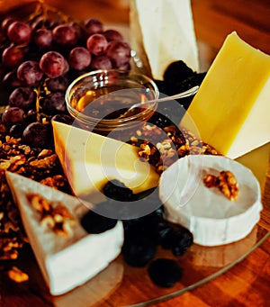 Cheese platter with different cheeses, grapes, nuts, honey, bread and dates on modern wooden background