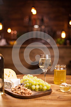 Cheese platter with fresh grapes and glasses of white wine on a rustic wooden table in a vintage pub.