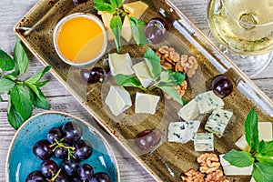 Cheese platter garnished with honey, walnuts, grapes, bread, mint and glass of wine over wooden background