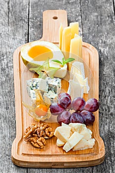 Cheese platter garnished with pear, honey, walnuts, grapes, carambola, physalis on cutting board