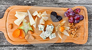 Cheese platter garnished with pear, honey, walnuts, grapes, carambola, physalis on cutting board on wooden background