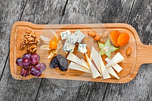 Cheese platter garnished with pear, honey, walnuts, grapes, carambola, physalis on cutting board on wooden background