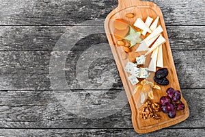 Cheese platter garnished with pear, honey, walnuts, grapes, carambola, physalis on cutting board on wooden background