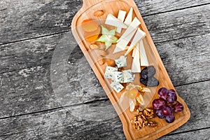 Cheese platter garnished with pear, honey, walnuts, grapes, carambola, physalis on cutting board on wooden background