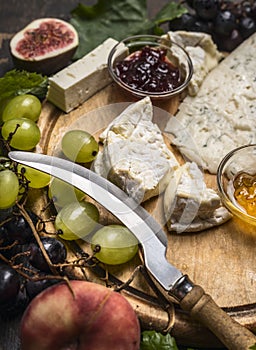 Cheese platter with Gorgonzola ,,Camembert and honey and jam, light and dark grapes peaches, knife for cheese on wooden cutting bo