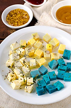 Cheese platter, Gouda, feta, blue pesto cheeses on white plate with herbs, olive oil, pomegranate and mustard sauces