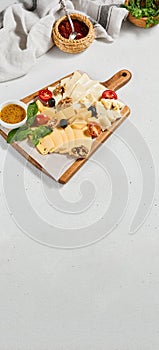 Cheese platter with nuts, honey sauce and olives on wood board. Cheeseboard on white concrete background. Cheese assorted in