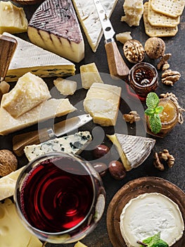 Cheese platter with organic cheeses, fruits, nuts and wine on stone background. Top view. Tasty cheese starter