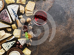 Cheese platter with organic cheeses, fruits, nuts and wine on stone background. Top view. Tasty cheese starter