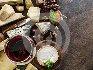 Cheese platter with organic cheeses, fruits, nuts and wine on stone background. Top view. Tasty cheese starter