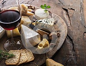 Cheese platter with organic cheeses, fruits, nuts and wine on wooden background. Tasty cheese starter
