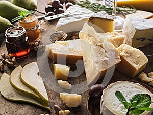 Cheese platter with organic cheeses, fruits, nuts and wine on wooden background. Tasty cheese starter