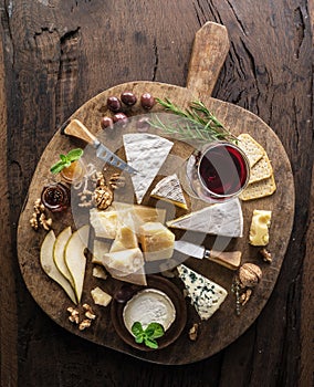 Cheese platter with organic cheeses, fruits, nuts and wine on wooden background. Top view. Tasty cheese starter