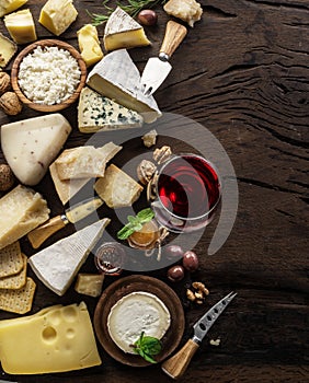 Cheese platter with organic cheeses, fruits, nuts and wine on wooden background. Top view. Tasty cheese starter