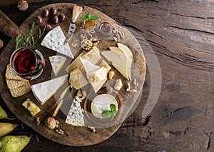 Cheese platter with organic cheeses, fruits, nuts and wine on wooden background. Top view. Tasty cheese starter