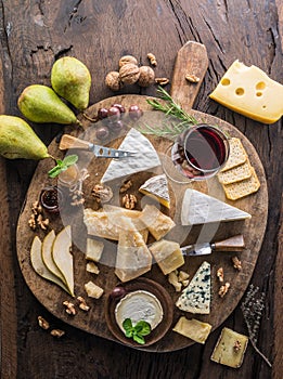 Cheese platter with organic cheeses, fruits, nuts and wine on wooden background. Top view. Tasty cheese starter