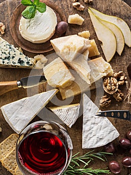 Cheese platter with organic cheeses, fruits, nuts and wine on wooden background. Top view. Tasty cheese starter