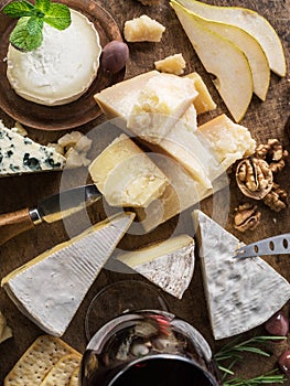 Cheese platter with organic cheeses, fruits, nuts and wine on wooden background. Top view. Tasty cheese starter