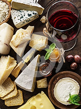 Cheese platter with organic cheeses, fruits, nuts and wine on wooden background. Top view. Tasty cheese starter