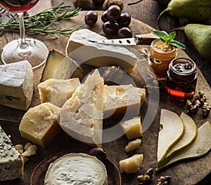 Cheese platter with organic cheeses, fruits, nuts and wine on wooden background. Top view. Tasty cheese starter