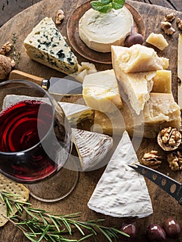 Cheese platter with organic cheeses, fruits, nuts and wine on wooden background. Top view. Tasty cheese starter