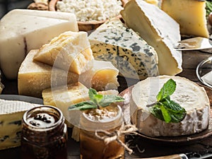 Cheese platter with organic cheeses, fruits, olives and jam on wooden background. Tasty cheese starter