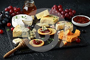 Cheese platter served with grapes, ale chutney, honey, crackers on stone board. Brie, cheddar, red leicester