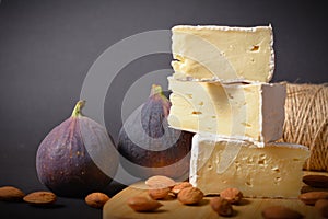 Cheese platter of Soft French Brie cheese cuts served with almond nuts and fig berries on wooden board