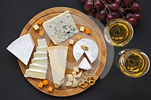 Cheese platter with wine, grapes, pretzels and walnuts on dark background, from above.Top view.